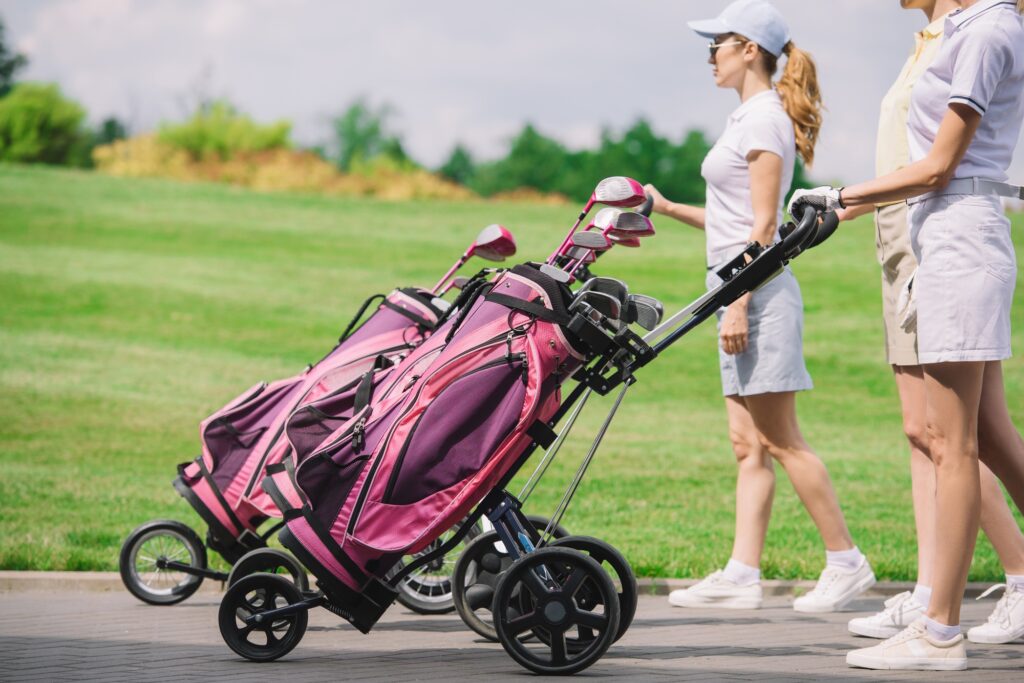 partial view of female golfers with golf equipment walking at golf course