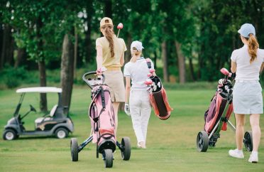 back view of women with golf gear walking on green lawn at golf course