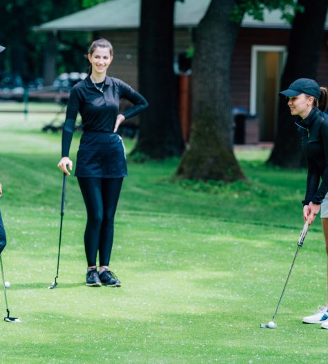 Golf putting lesson, two young female golfers practicing putting with golf instructor