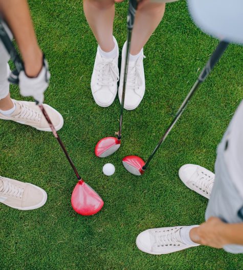 overhead view of female golf players with golf clubs standing on green lawn with golf ball in middle